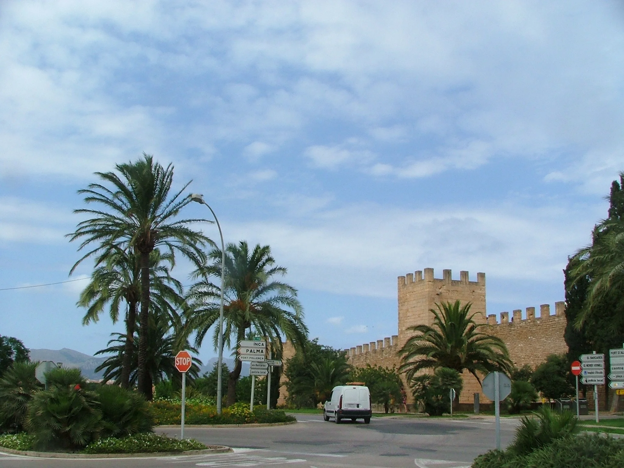 The medieval walls of Alcudia old town with a sandstone watchtower against a blue sky